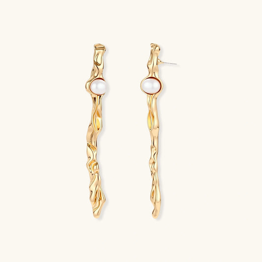 Long gold twisted sculptural earrings with round pearls, featuring flowing organic design on cream background