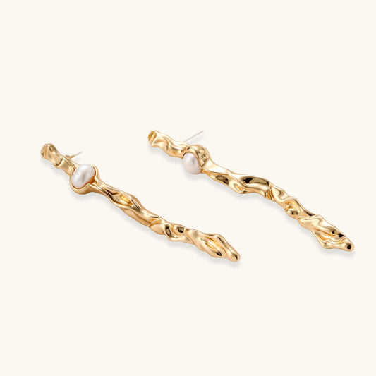 Long gold twisted sculptural earrings with round pearls, featuring flowing organic design on cream background