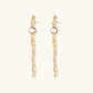 Long gold twisted sculptural earrings with round pearls, featuring flowing organic design on cream background