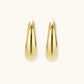 Chunky gold-plated sterling silver huggie hoop earrings with hinged closure mechanism on cream background.