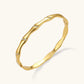 Gold-toned wavy bangle with bamboo-style segments and CZ crystal clusters on cream background. 18K plated stainless steel.